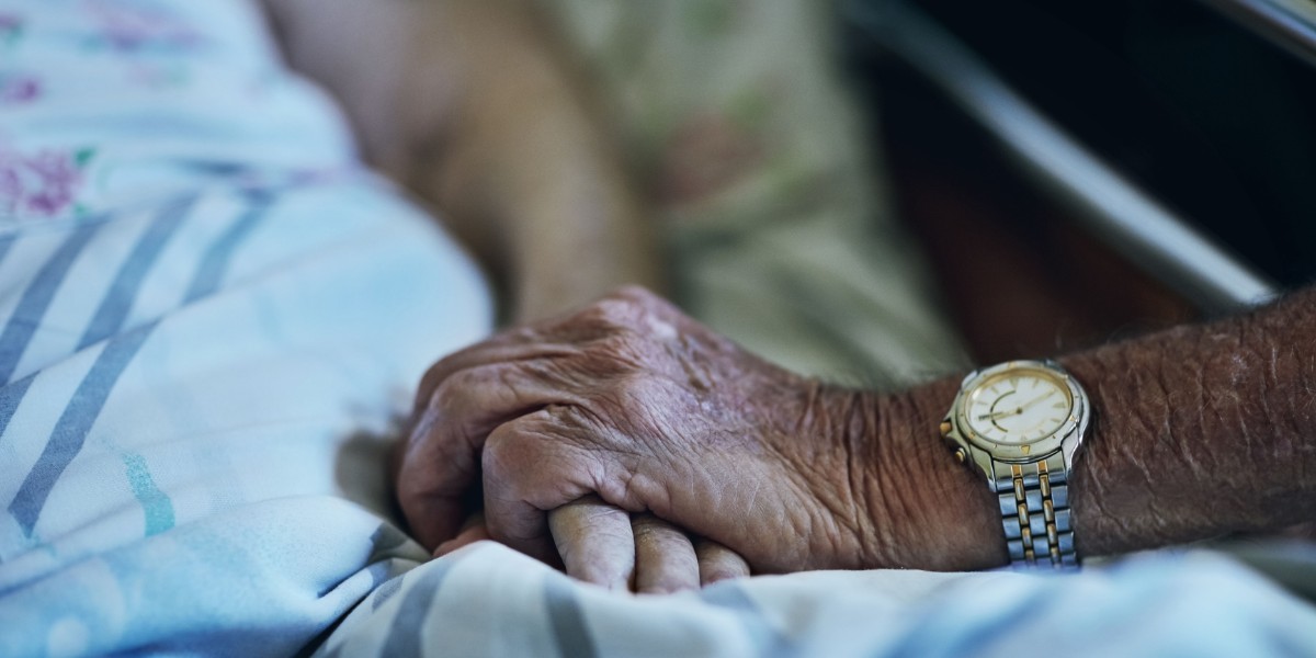 Old man holding the hand of a sick companion.