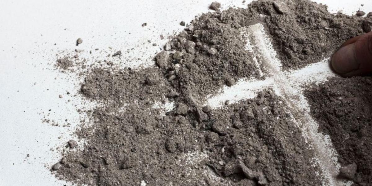 Finger drawing a cross shape in a pile of ashes.