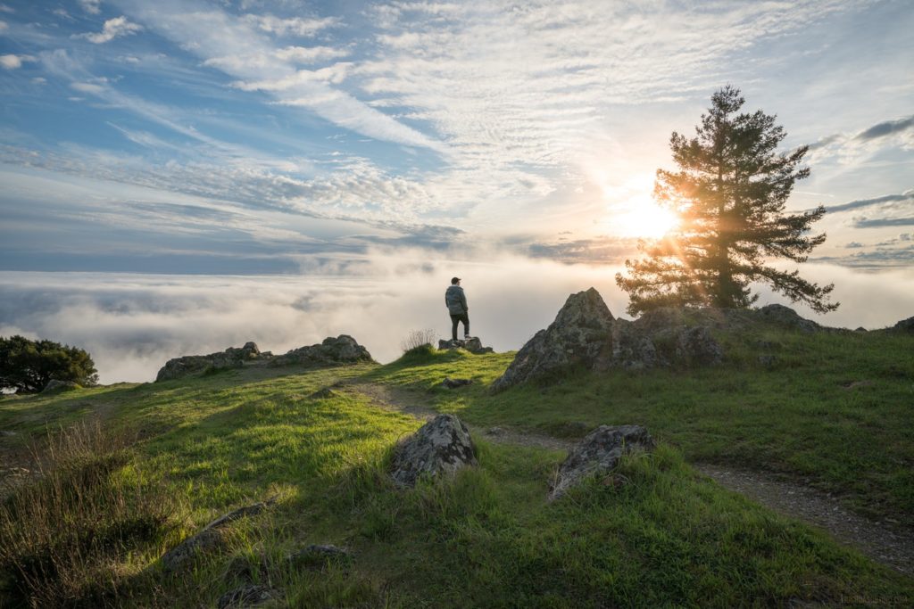 Person standing by the edge of a tall mountain looking down at the view.