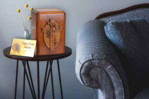 Wooden cremation urn on stand next to couch.
