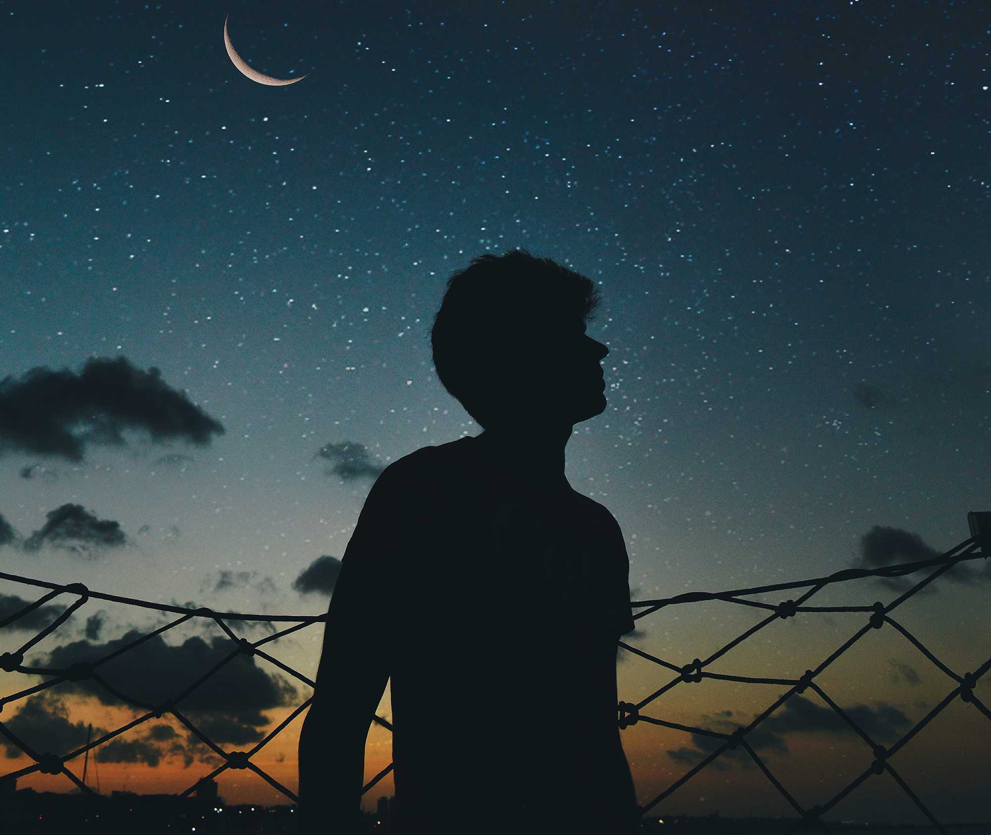 Shadow of a man looking at the night sky with stars and the moon behind him.