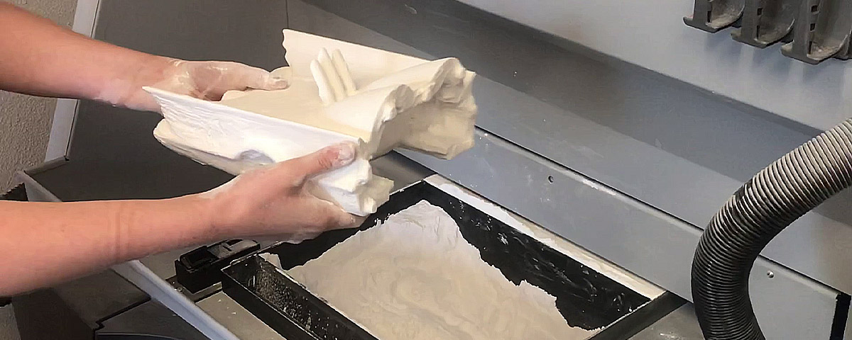 Half of the printed car model being taken out of the 3D printer powder bed.