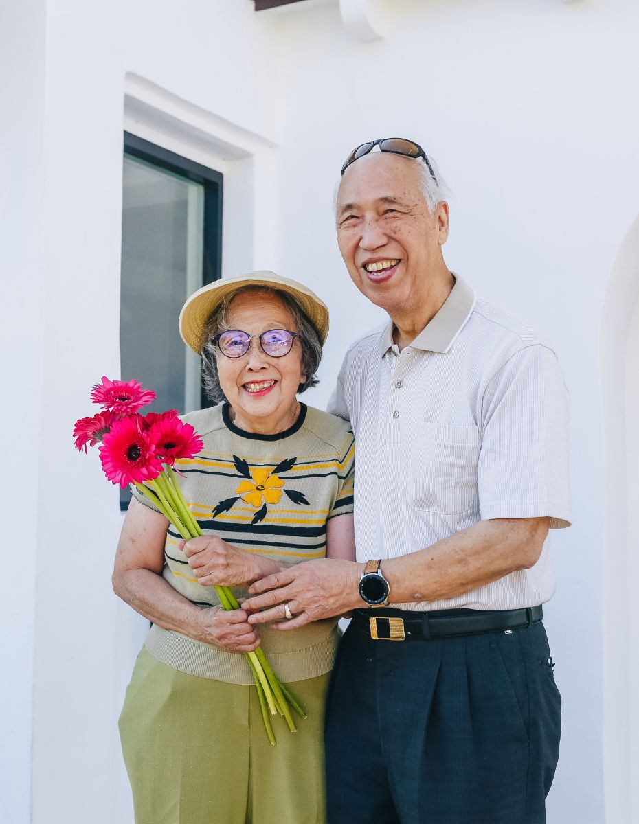 Elderly couple standing on their porch smiling at the camera.