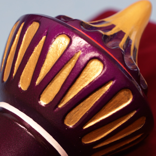 A close-up of the cap of the 3D-printed genie bottle painted in violet-red and gold.