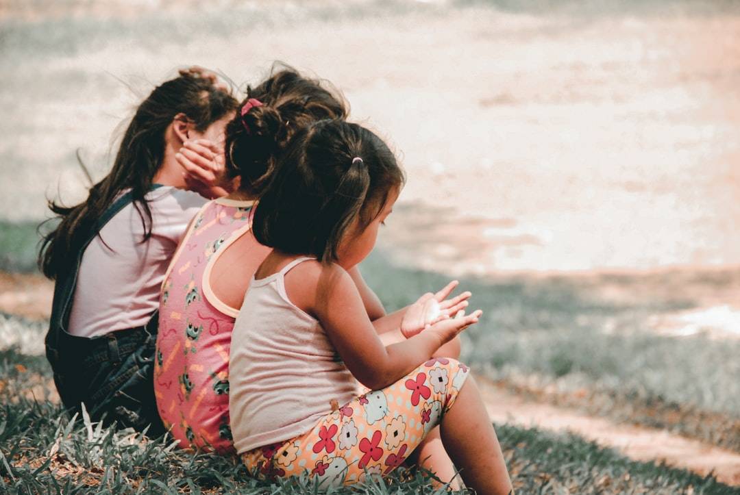 Three young girls sitting together in the grass.