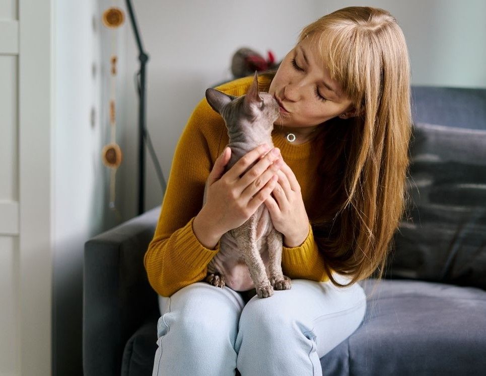 Woman sitting on the couch kissing a cat.