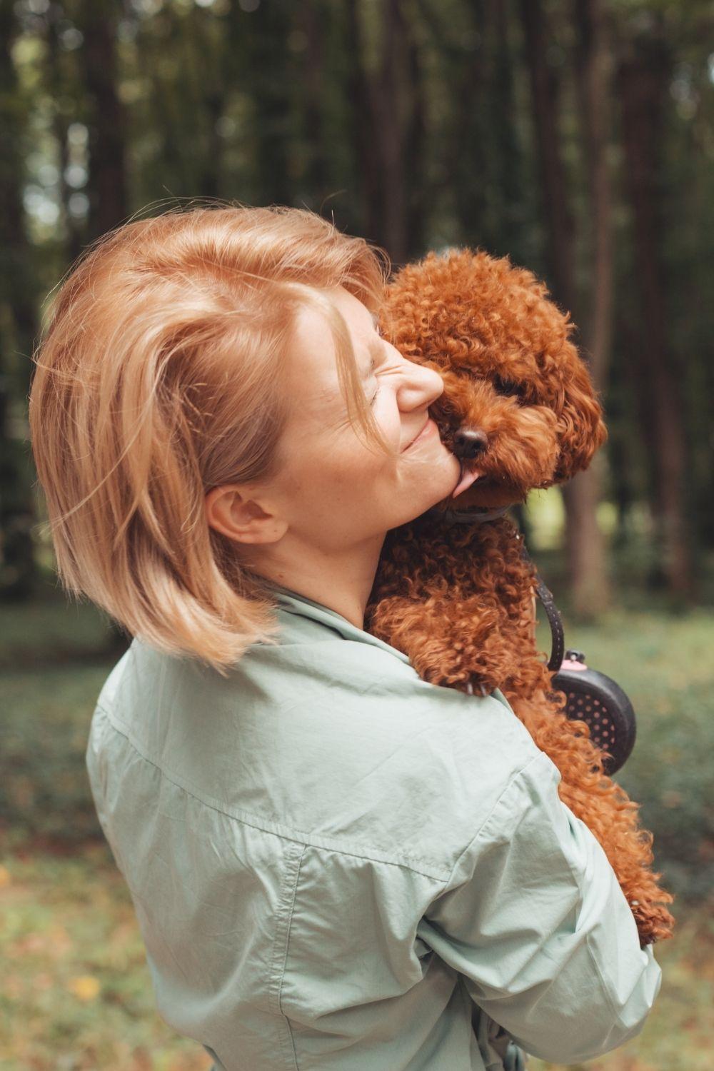 Woman holding a puppy in her arms while it licks her face.