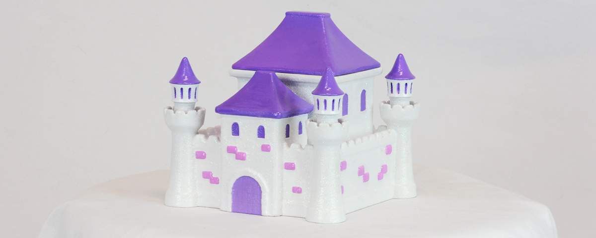 A 3D-printed custom cremation urn in the shape of a princess castle, with white and pink walls and purple roofs.