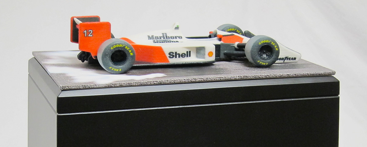 A 3D-printed McLaren-Honda Formula 1 car decorates the top of a black wooden urn.