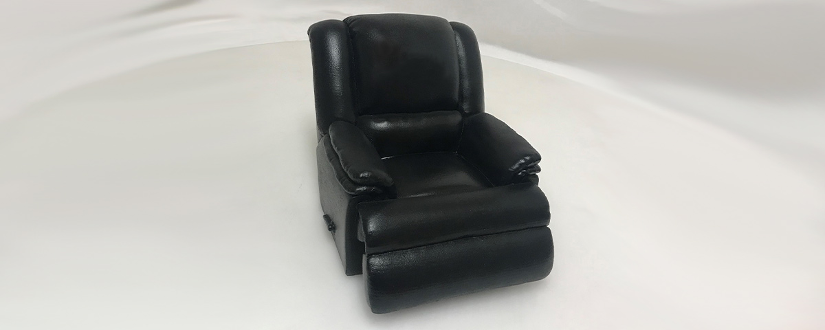 A 3D-printed custom cremation urn resembling a black leather recliner. The urn is keepsake-sized.