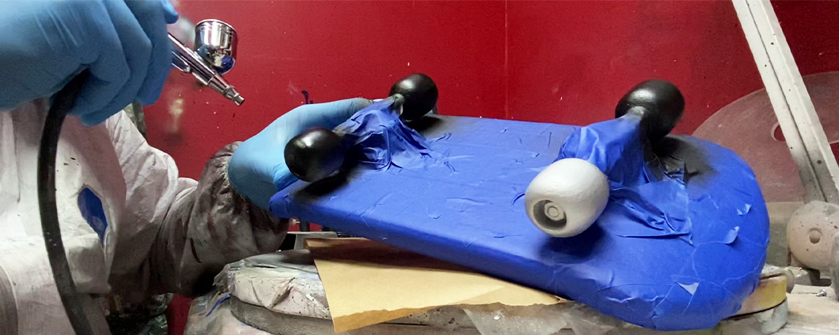 The 3D-printed skateboard urn base covered in painter's tape and being airbrushed with black paint.